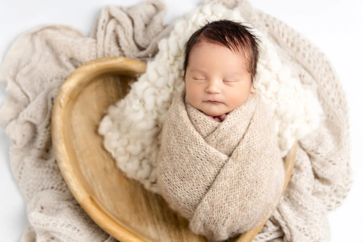 Newborn baby wrapped in soft beige knit blanket sleeping peacefully in wooden bowl, professional newborn photography Hartlepool